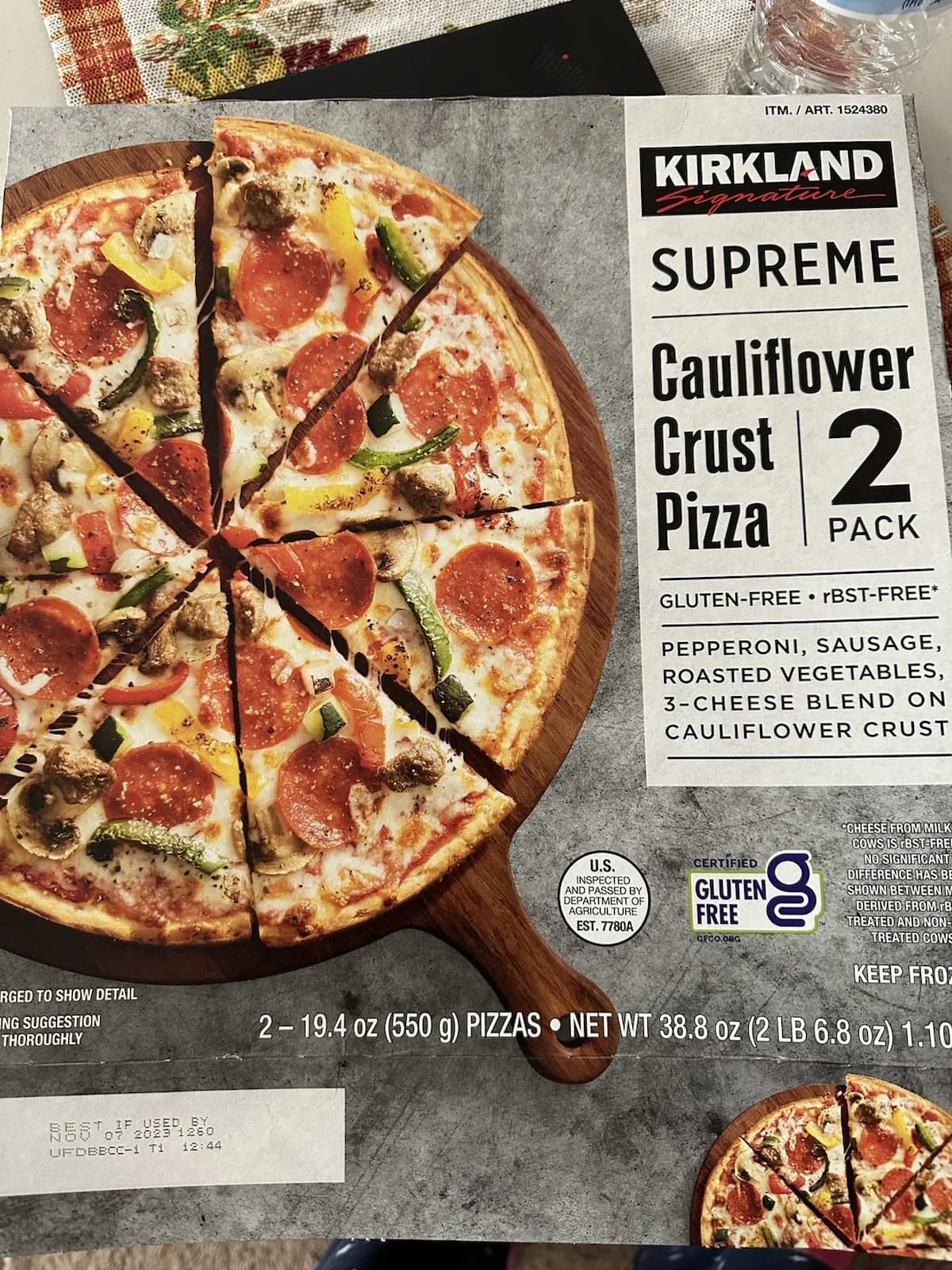 A box of Kirkland Signature Supreme Cauliflower Crust Pizza, 2-pack, featuring an image of a sliced pizza with pepperoni, sausage, roasted vegetables, and a 3-cheese blend on a wooden board. Gluten-free is indicated.