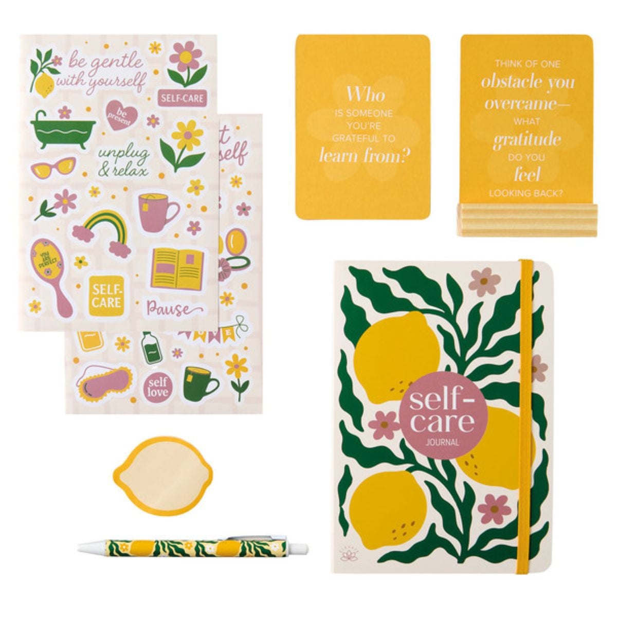 A self-care-themed stationery set with stickers, journal, cards, a pen, and a sticky note pad. Designs feature lemons, flowers, and encouraging words in yellow, green, and pink colors.