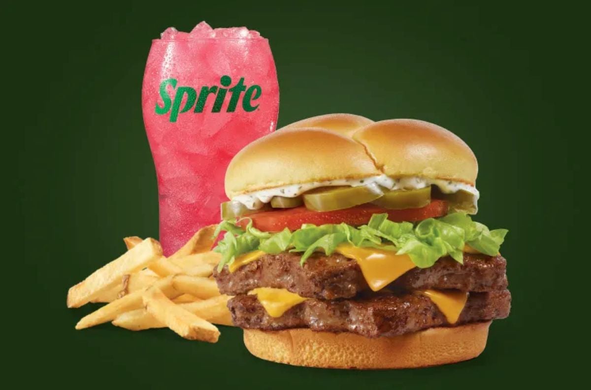Experience the new fast-food menu with a cheeseburger featuring lettuce, tomato, pickles, and two beef patties, served alongside crispy fries and a pink Sprite in a clear cup—all set against a dark green background.