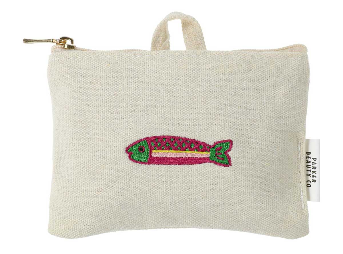 A small, square, off-white fabric pouch with a zipper and top handle. Featuring an embroidered pink and green fish, this charming design is inspired by new Five Below products and includes a white Parker Beauty Co. tag on the side.