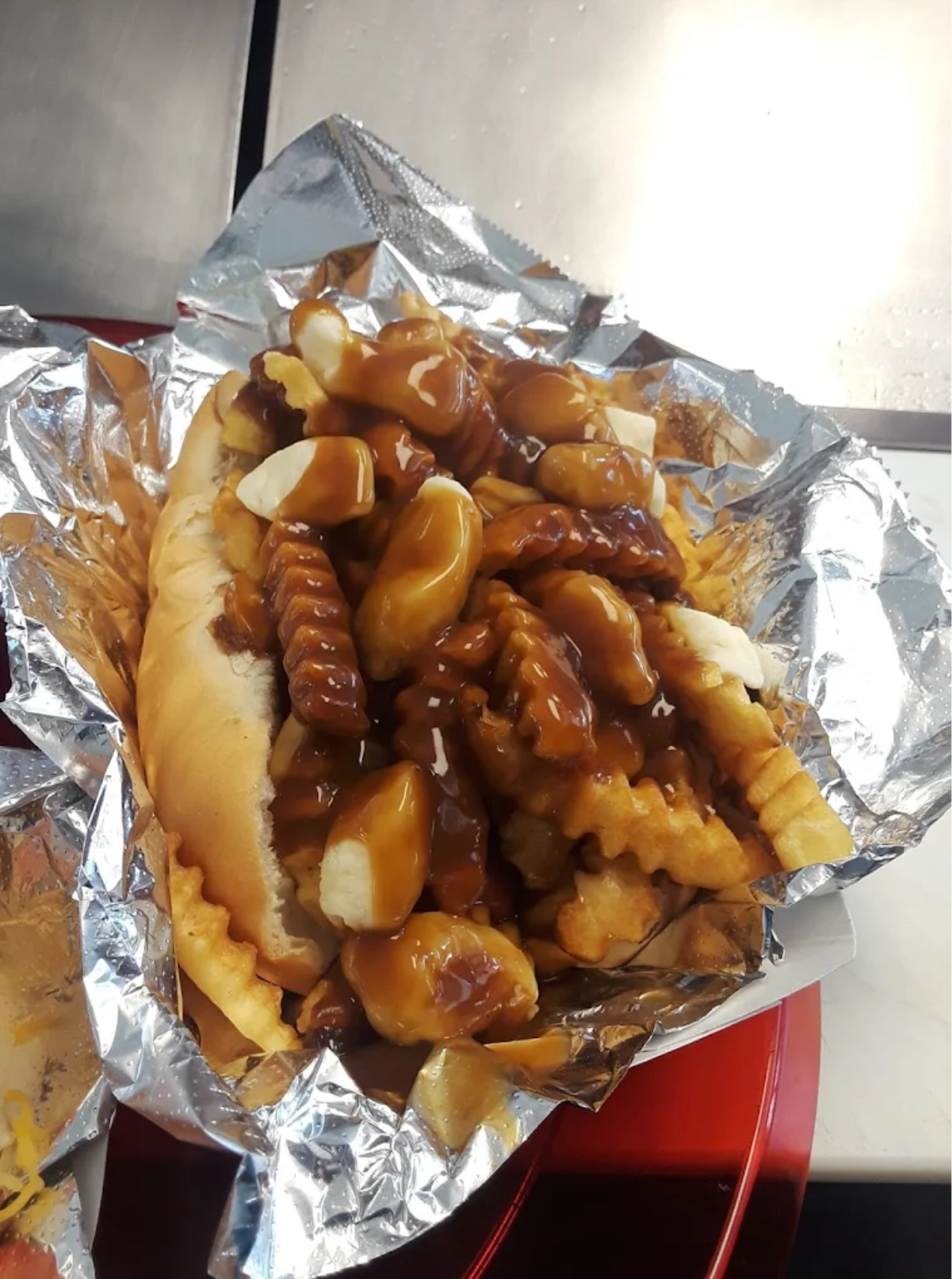 A hot dog topped with crinkle-cut fries, cheese curds, and brown gravy, served on a foil-lined tray.
