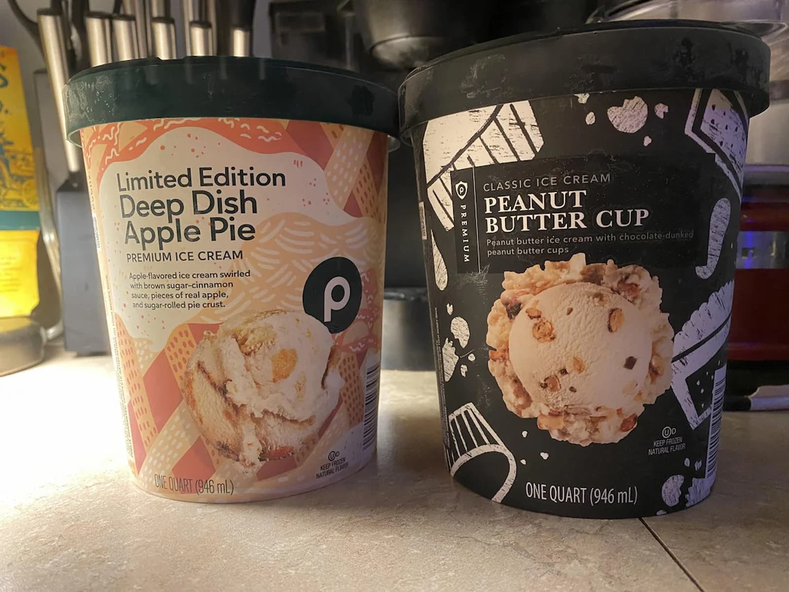 Two cartons of Publix ice cream on a kitchen counter: one is Limited Edition Deep Dish Apple Pie flavor, the other is Classic Peanut Butter Cup flavor. Both cartons are one quart in size.