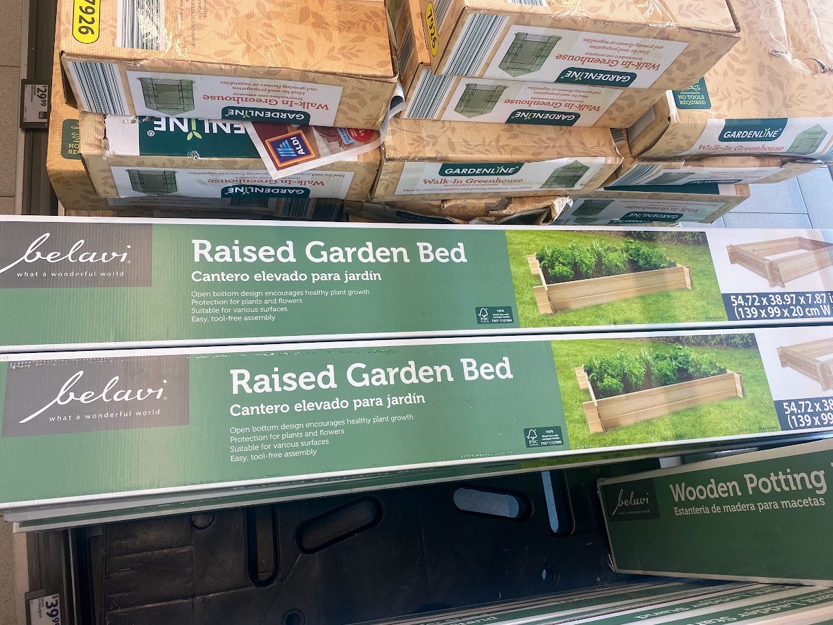 Two boxed kits labeled "Raised Garden Bed" in English and Spanish are stacked on a store shelf. The boxes show an image of the garden bed and the dimensions 54.7 x 23.8 x 9.1 inches (139 x 60.47 x 23 cm).