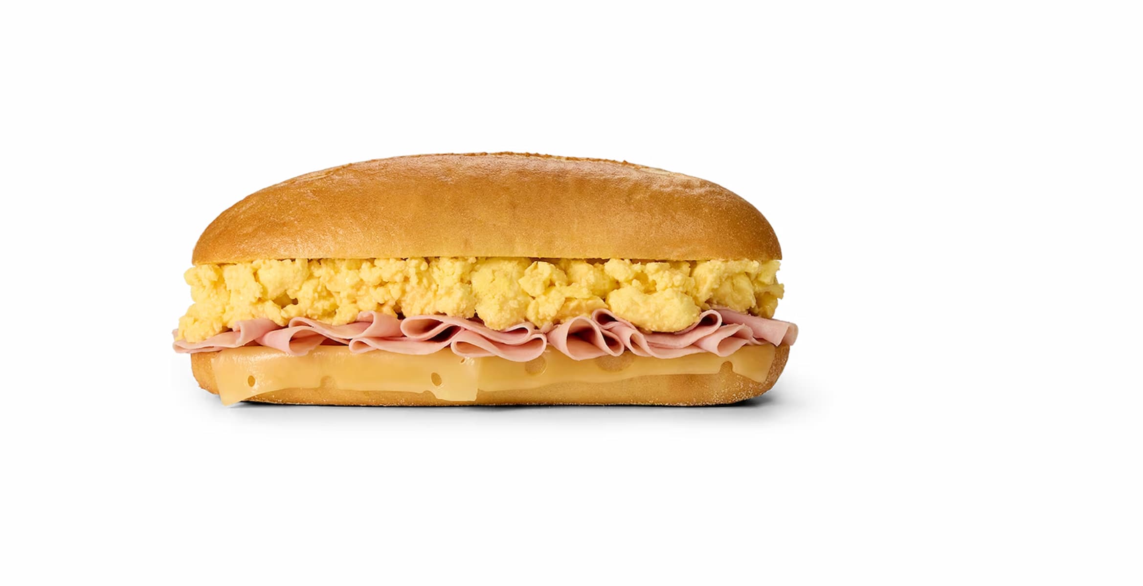 A breakfast sandwich on a bun, filled with layers of scrambled eggs, sliced ham, and Swiss cheese, shown on a plain white background.