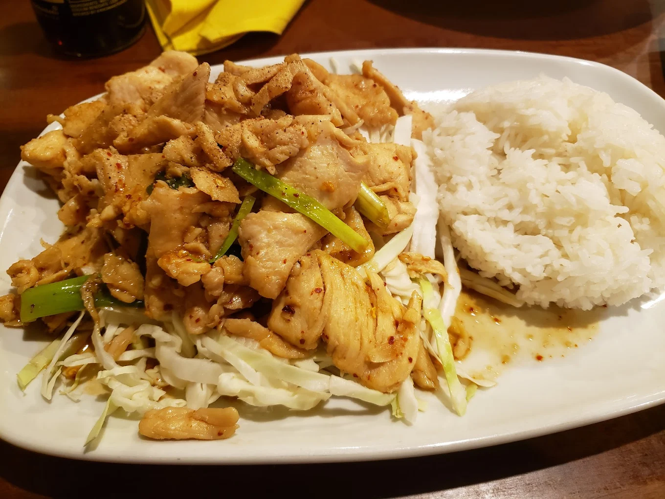 A white plate with stir-fried chicken, green onions, and cabbage in a savory sauce, served next to a mound of steamed white rice.