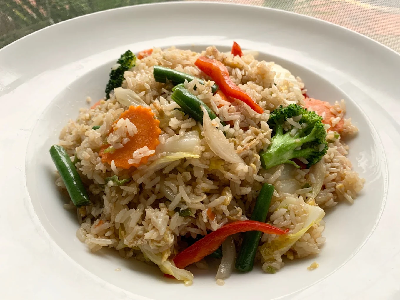 A plate of vegetable fried rice with broccoli, carrots, green beans, cabbage, and red bell peppers, served on a white dish.