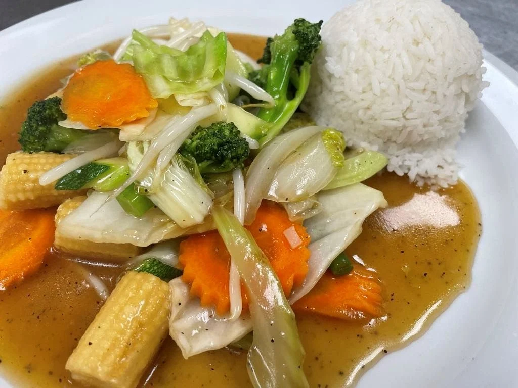 A plated dish of stir-fried mixed vegetables in brown sauce, including broccoli, baby corn, carrots, and cabbage, served with a mound of white rice.