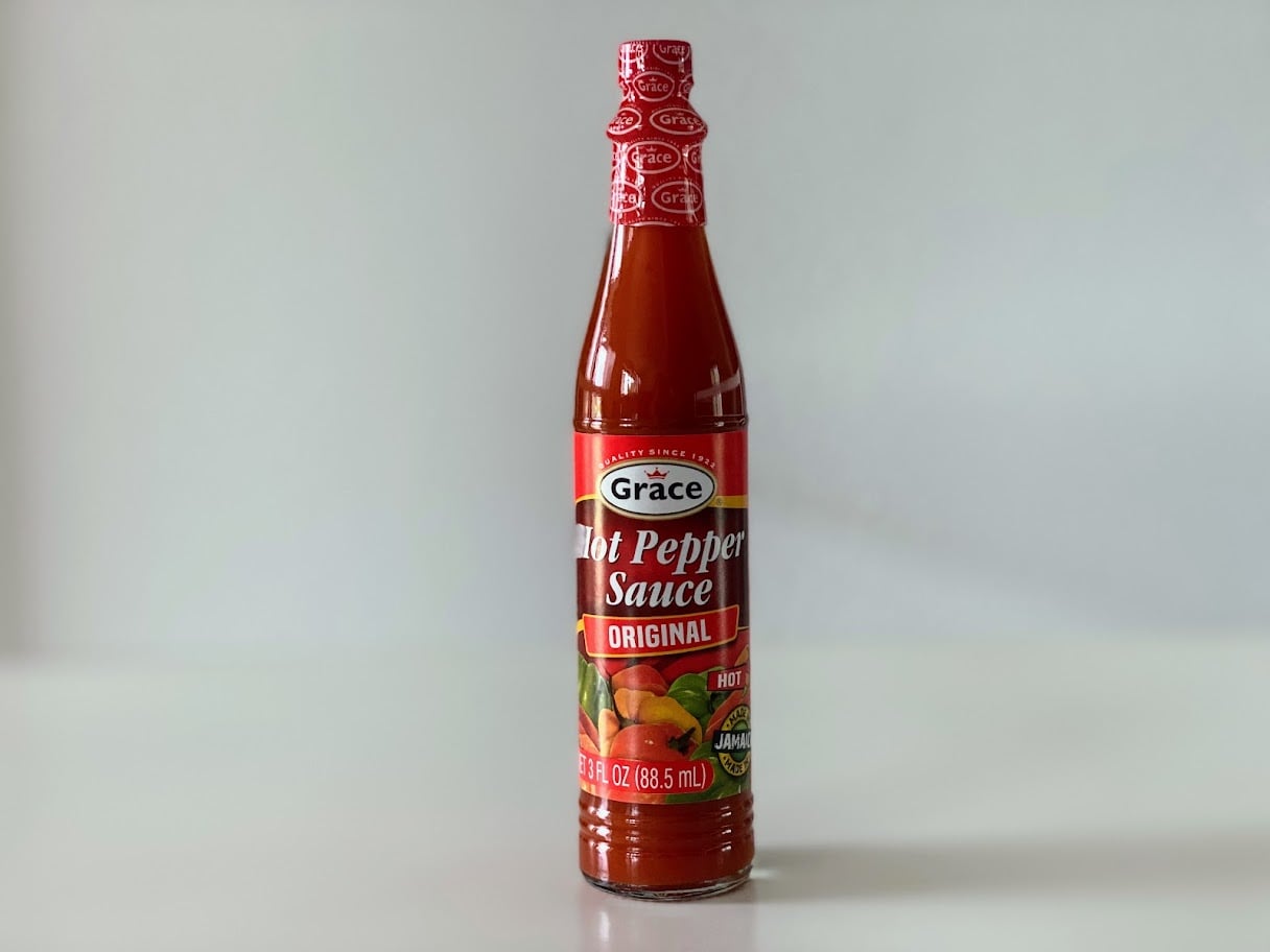 A bottle of Grace Hot Pepper Sauce Original with a red cap and label, featuring images of peppers and text indicating it is 12 oz (345 mL) and rated as hot. The bottle sits on a white surface.
