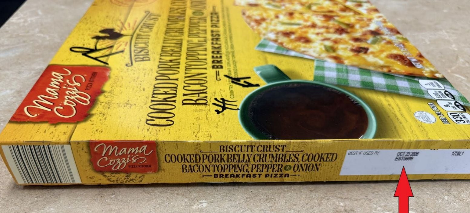 A Mama Cozzi's Breakfast Pizza box on a counter, featuring biscuit crust, pork belly crumbles, bacon, pepper, and onion. A red arrow points to the "Best if used by" date printed on the side of the box.