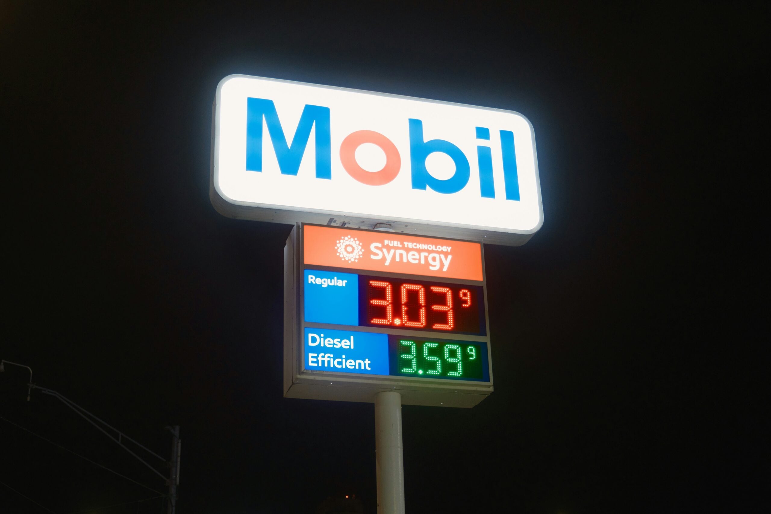 Mobil gas station sign at night displaying fuel prices: Regular at $3.03 and Diesel at $3.59. The sign is brightly lit against a dark sky.