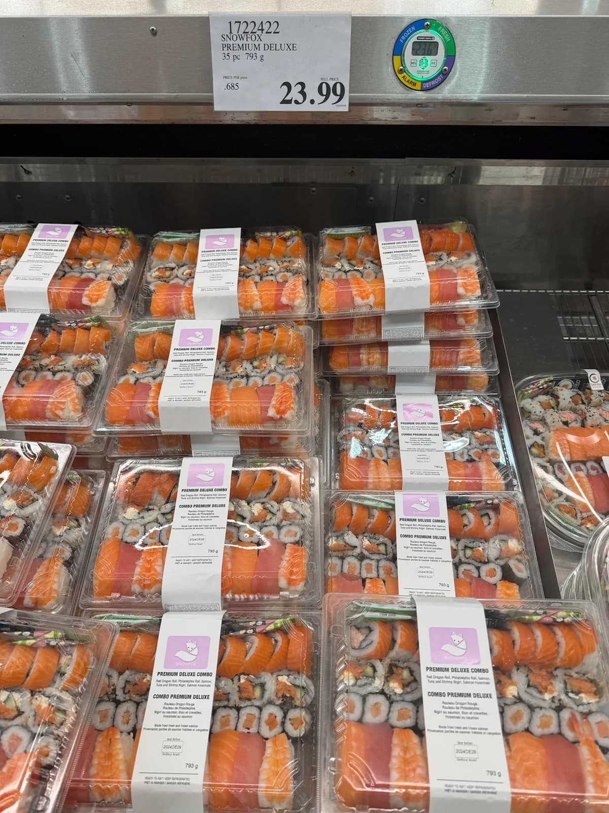 A display of Snowfox Premium Deluxe sushi combos for $23.99. Multiple clear plastic containers filled with various sushi rolls, some with salmon, tuna, and other ingredients.