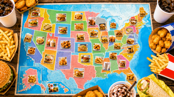 A colorful map of the United States displays photos of fast food items from iconic fast food places in each state. Surrounding the map are drinks, fries, a burger, tater tots, fried chicken, a wrap, and a dessert on a wooden table.