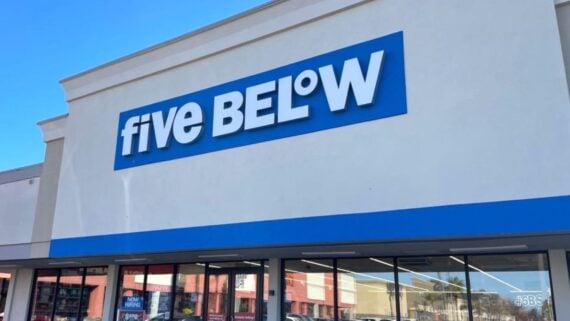 The front of a Five Below store with a large blue and white sign above the entrance, set against a clear blue sky&mdash;perfect for your first time at Five Below.