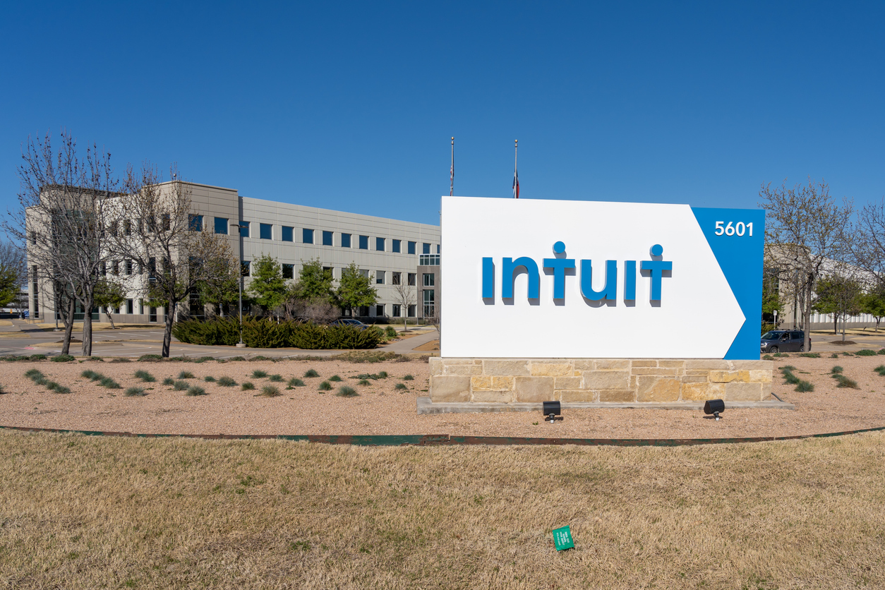A large outdoor sign with the Intuit logo and the number 5601 stands in front of a modern office building, surrounded by a grassy area and small trees, as news of 2026 layoffs circulates under a clear blue sky.