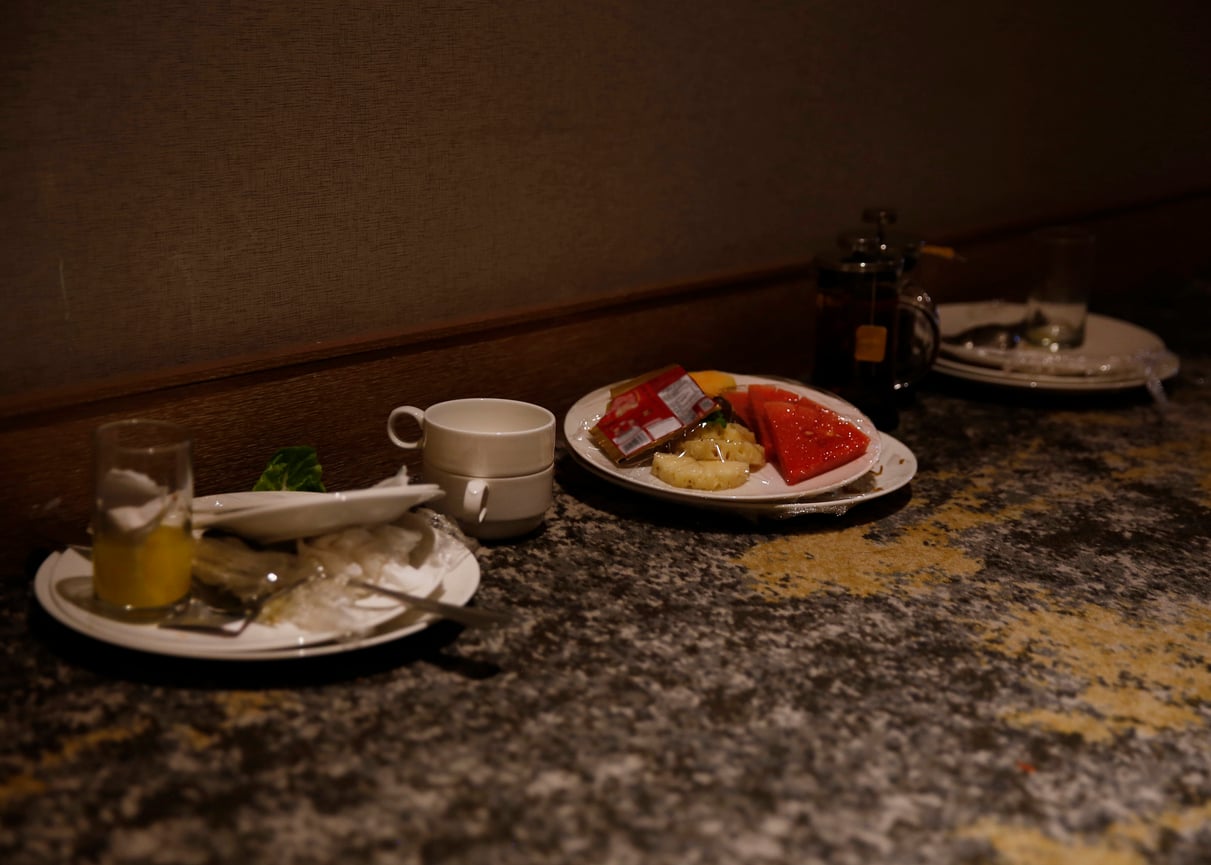 Three plates with leftover food, a glass, a teapot, and cups sit on a speckled countertop against a brown wall, highlighting the importance of hotel room etiquette after enjoying a meal.