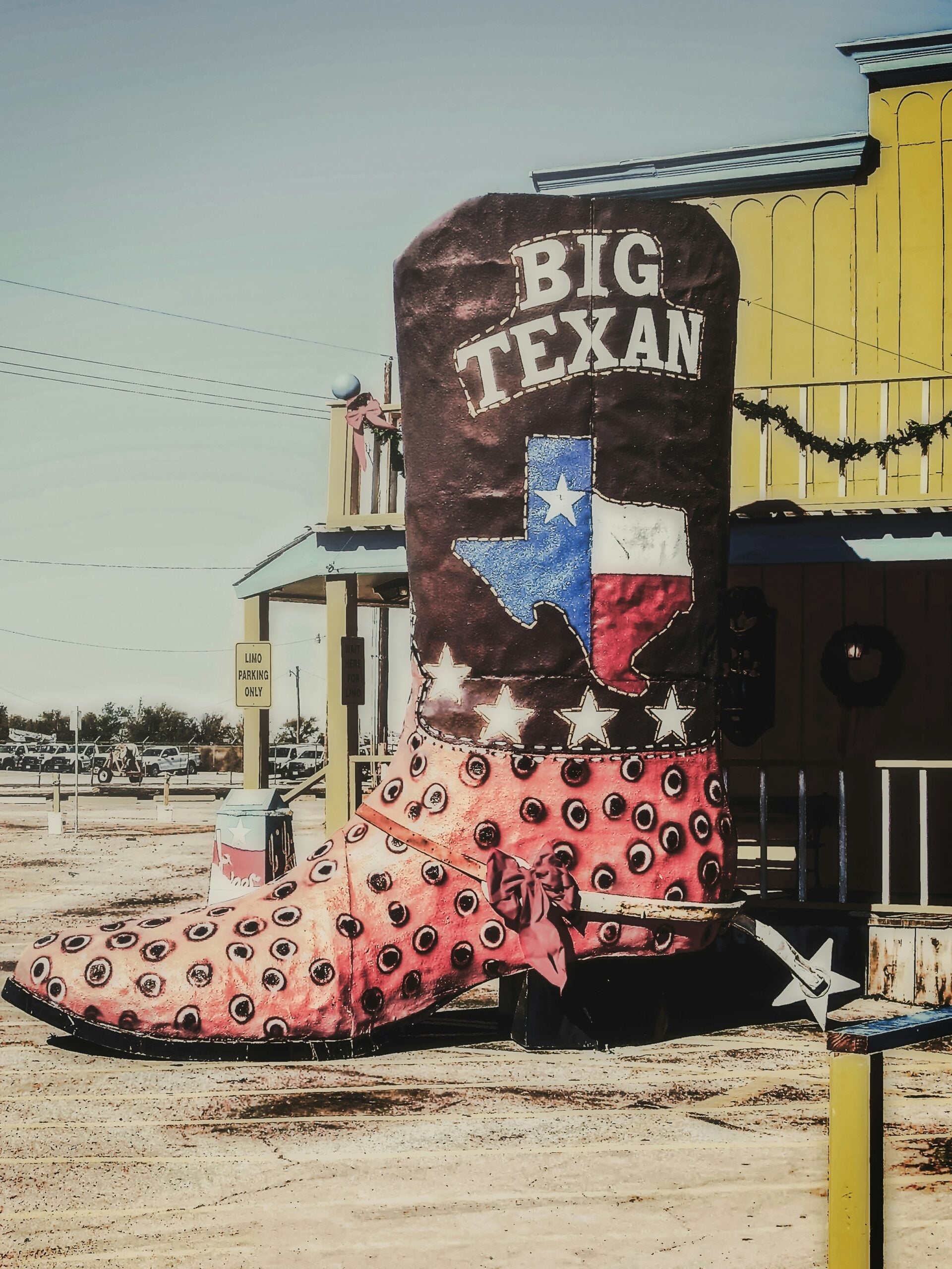 A giant cowboy boot statue with "BIG TEXAN" and a Texas flag design stands outside a yellow western-style building under a clear sky.