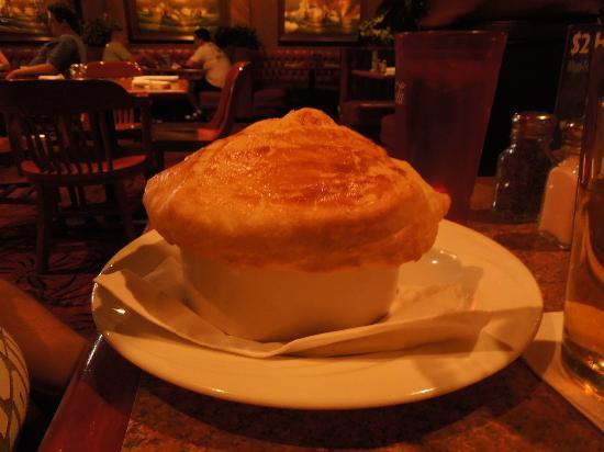 A white bowl with golden-brown puff pastry on top, served on a white plate in a restaurant with dim lighting and red chairs in the background.