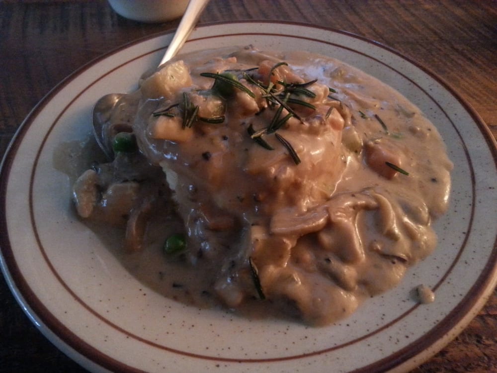 A plate of savory chicken and vegetables covered in creamy mushroom gravy, garnished with rosemary, on a white plate with brown trim.