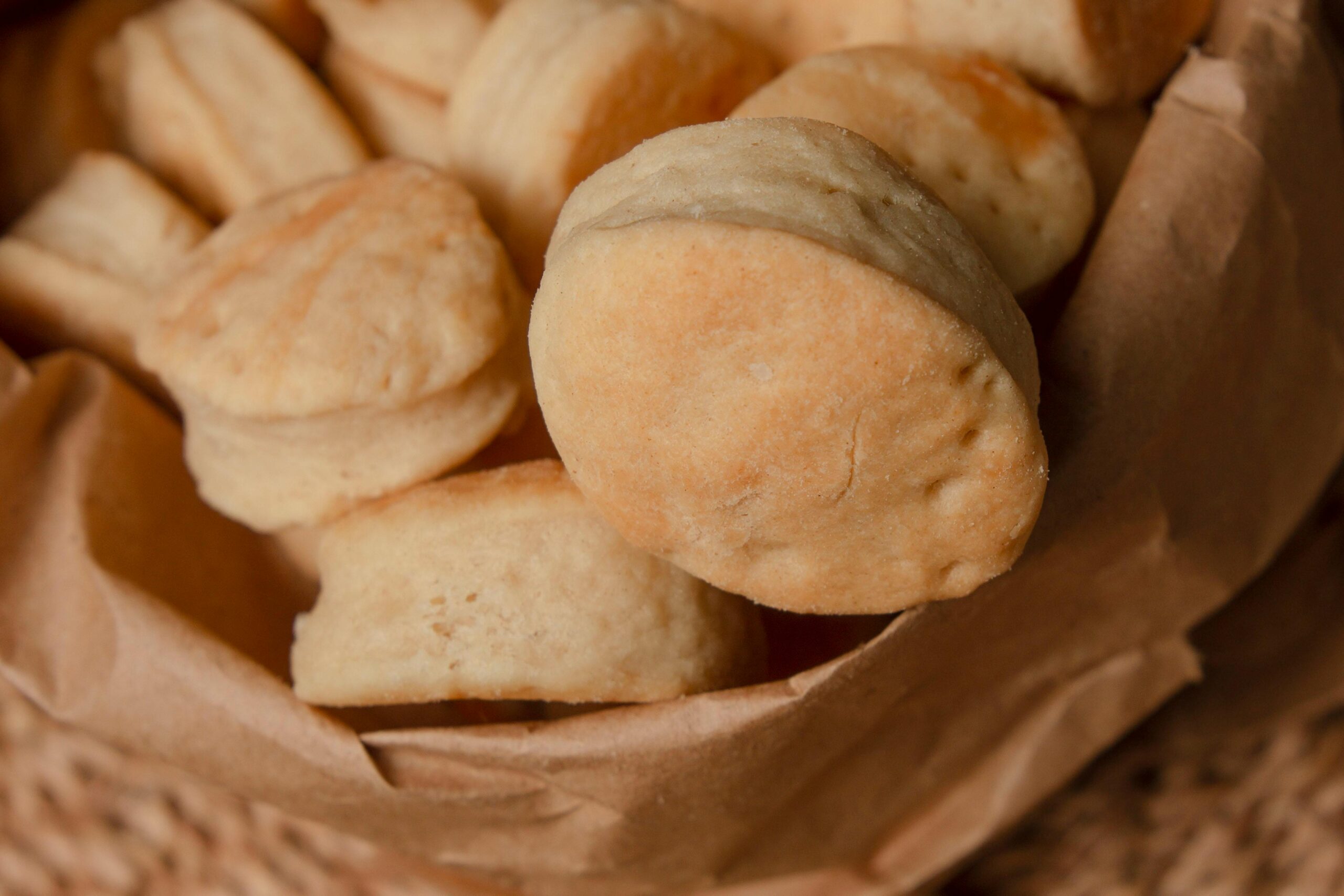 A close-up of several round, golden-brown biscuits or scones in a brown paper wrapper, showcasing their soft and slightly crumbly texture.