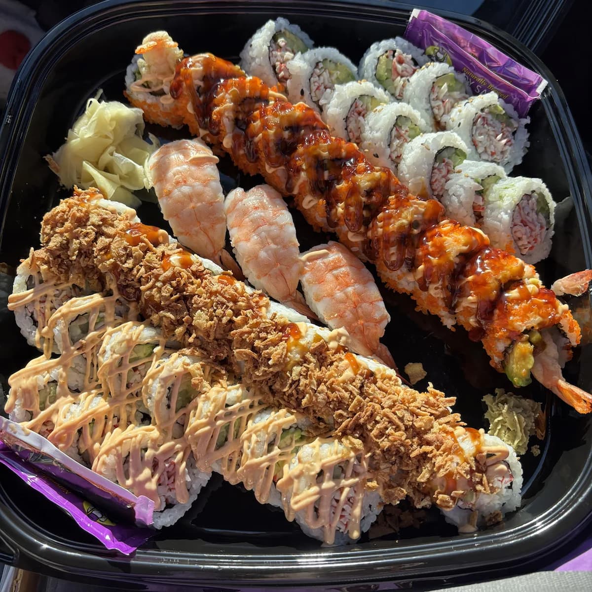 A large platter of assorted sushi rolls, including ones topped with crispy fried onions, a spicy sauce, and whole shrimp.