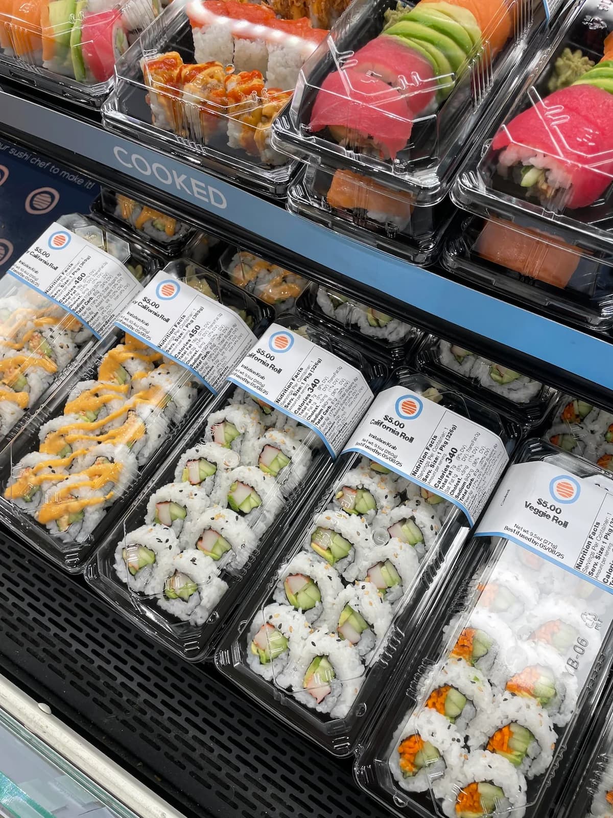 Assortment of pre-packaged sushi rolls, including California, spicy mayo, and veggie rolls, displayed in clear plastic containers with nutrition labels.