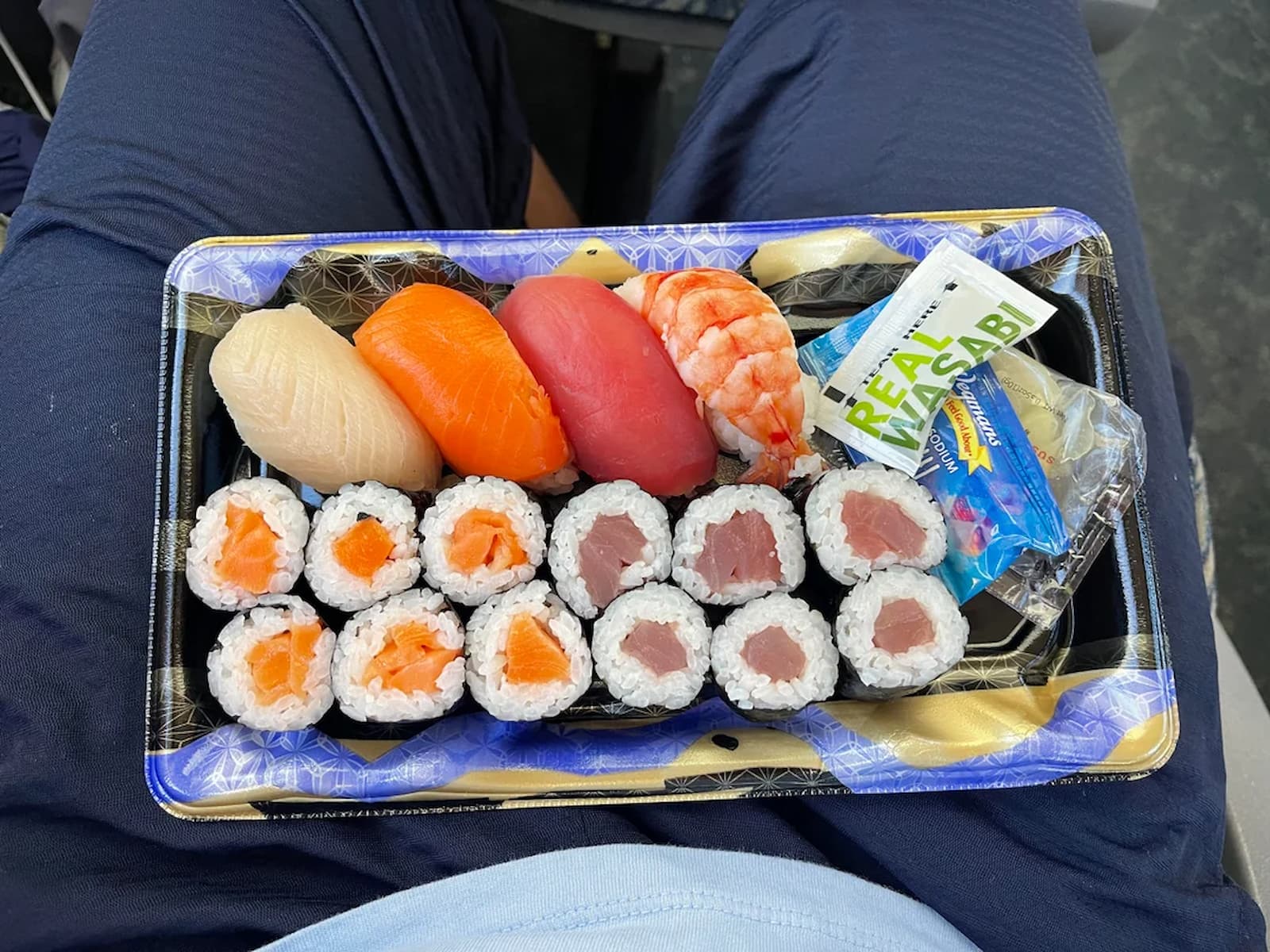 A tray of sushi with salmon, tuna, shrimp nigiri, and salmon and tuna rolls. Includes a packet of wasabi.