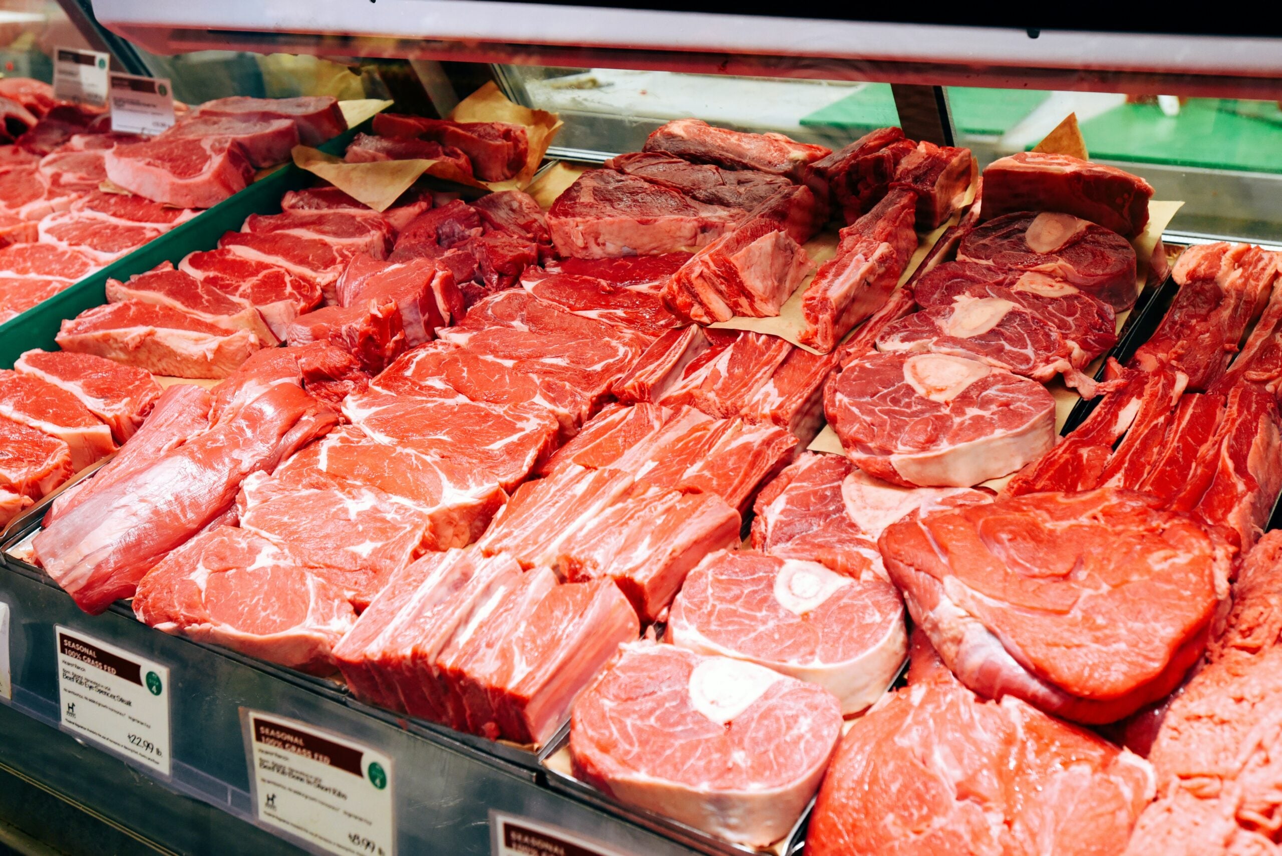Various cuts of raw red meat, including steaks and roasts, are displayed in a supermarket meat case on trays lined with paper, ready for purchase.