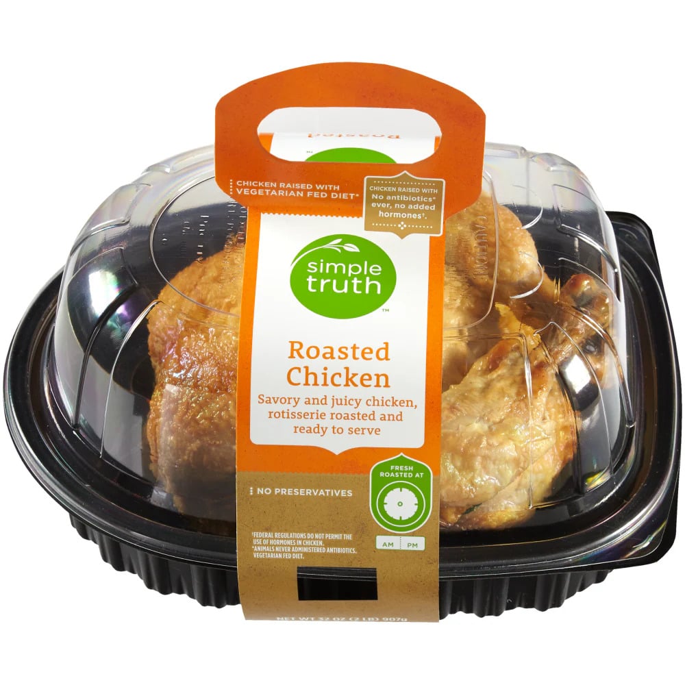 A plastic container with a handle holds a whole Rotisserie Chicken. The label reads “Simple Truth Roasted Chicken,” featuring product details and a note that it contains no preservatives.