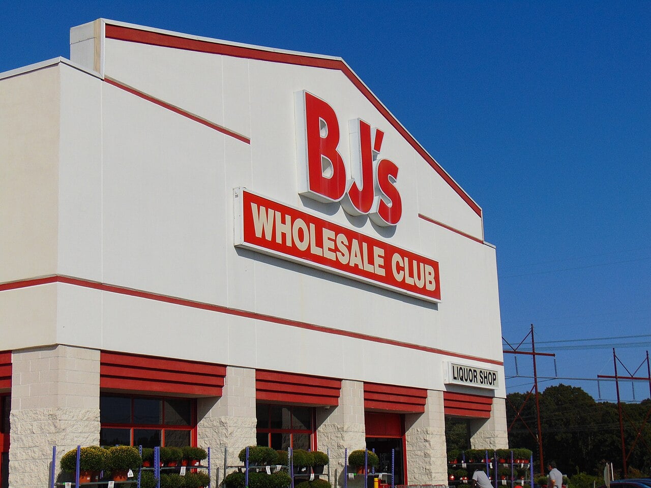 A large BJ's Wholesale Club store with a prominent red and white sign on the building; clear blue sky above and some greenery in front of the entrance.