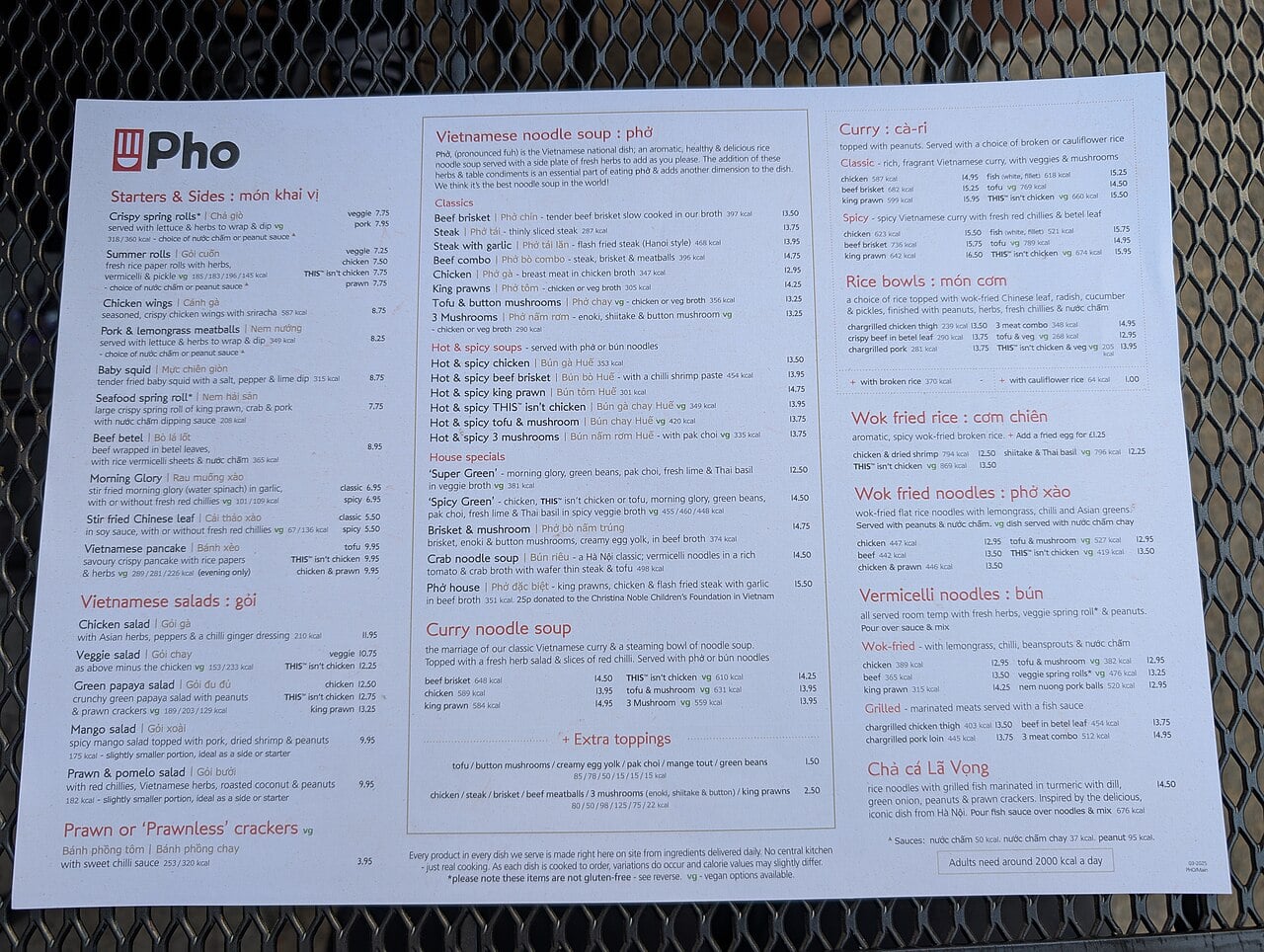 A Vietnamese restaurant menu displays various sections including starters, salads, noodle soups, curries, rice bowls, fried rice, vermicelli noodles, and beverages on a gray metal mesh table.