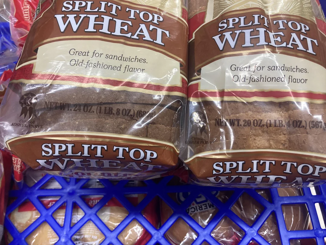 Two loaves of split top wheat bread in clear packaging with labels reading "Great for sandwiches. Old-fashioned flavor" in a blue shopping basket. The net weight is 20 oz (1 lb 4 oz) each.