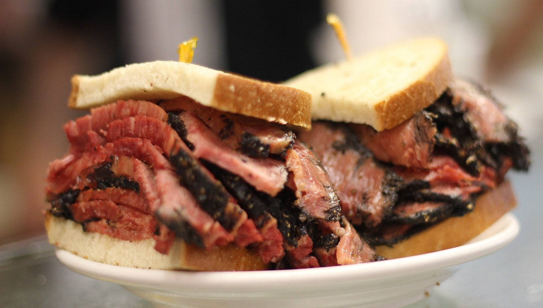 A close-up of two sandwiches filled with thick slices of pastrami between slices of white bread, served on a white plate—perfect for satisfying cravings at classic road trip food stops.