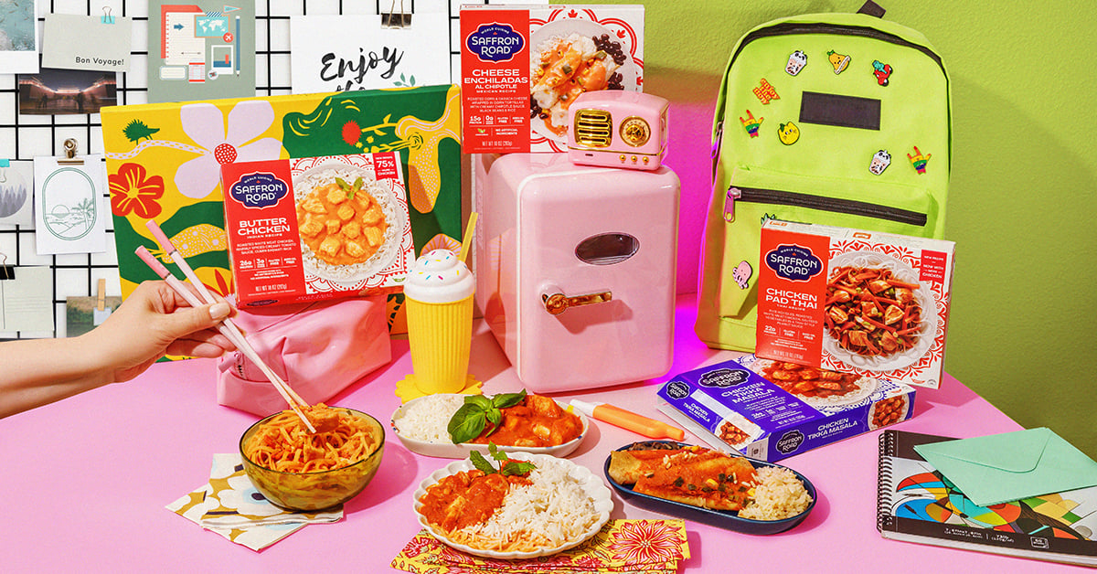 A colorful scene featuring Saffron Road frozen meals, a mini pink fridge, a green backpack with pins, notebooks, and various stationery on a pink table. Someone is holding chopsticks over delicious frozen meals in a bowl of noodles.