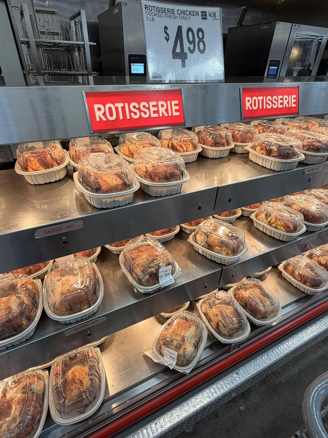Rows of Rotisserie Chicken are neatly displayed on heated shelves, with bold red “ROTISSERIE” signs and a large price sign advertising each chicken for just $4.98.