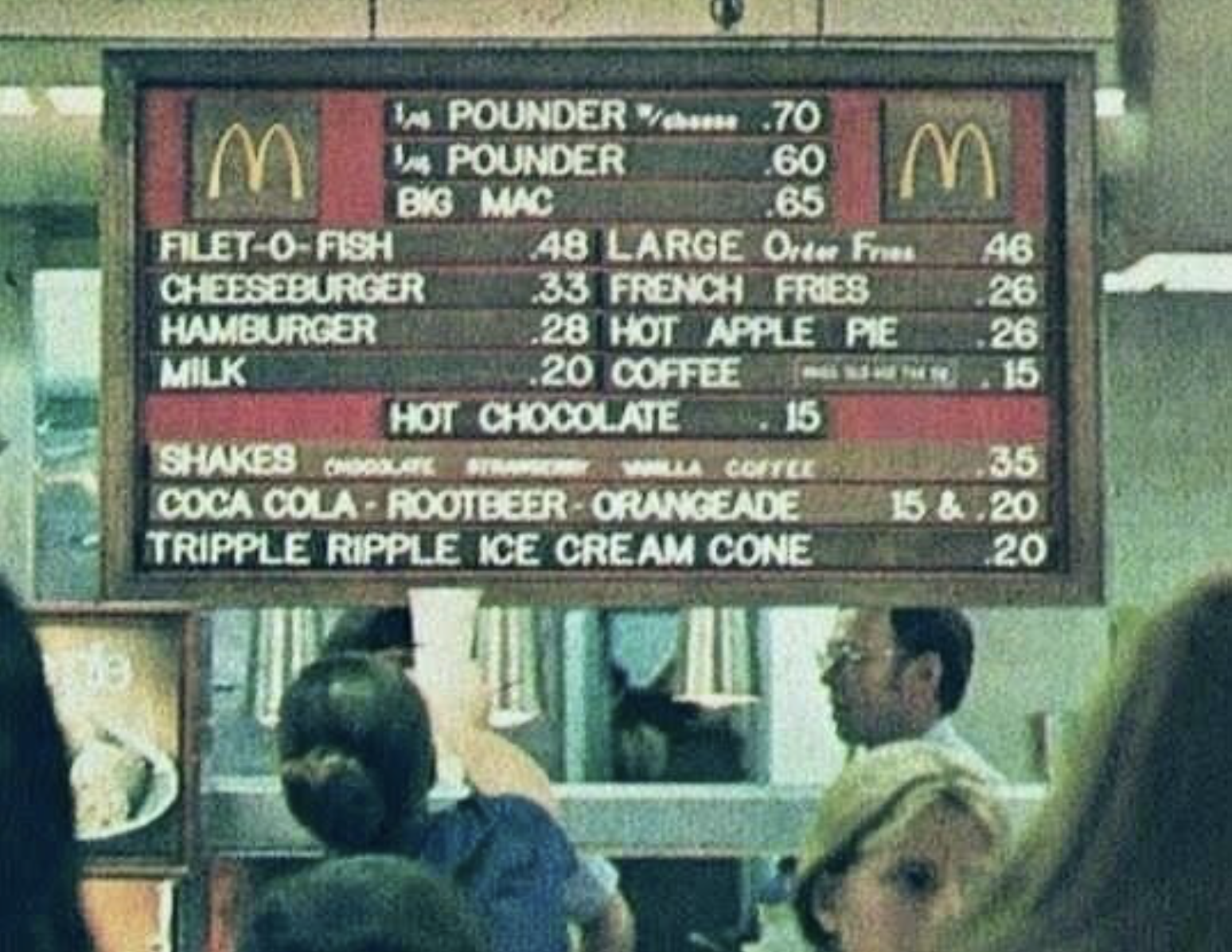 Vintage Fast-Food Photos: A classic McDonald's menu board displays prices for favorites like Filet-O-Fish, cheeseburgers, Big Macs, fries, shakes, drinks, and ice cream as customers gather at the counter below.