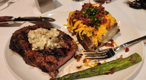 A grilled steak with seasoned butter, a baked potato topped with cheddar, bacon bits, and chives, plus a spear of asparagus&mdash;this classic plate could be found at many cheap steakhouses, served with a fork and steak knife.