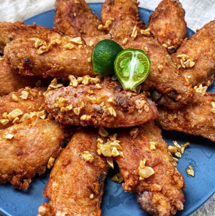 A plate of golden-brown fried chicken wings garnished with crispy garlic bits and a halved calamansi lime on top, perfect for pairing with your favorite wing sauces.
