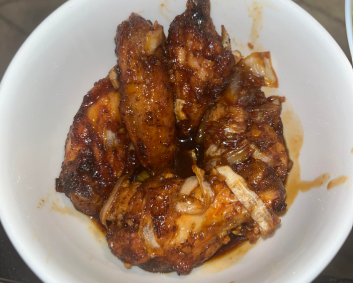 A white bowl filled with glazed chicken wings, garnished with chopped onions and coated in a dark, savory wing sauce.