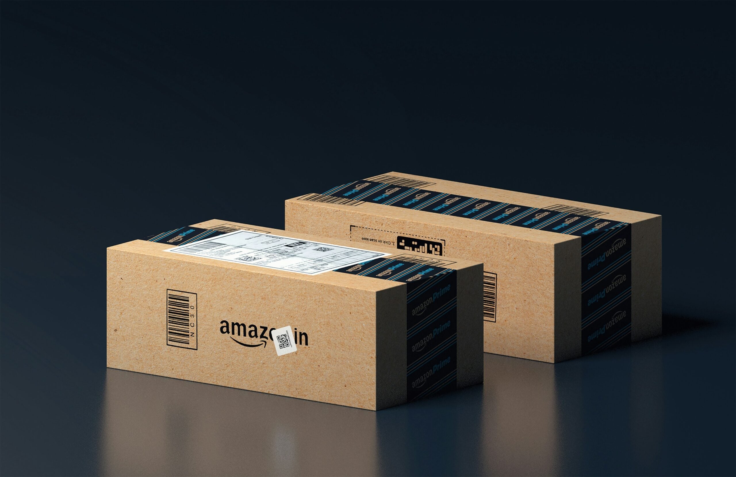 Two cardboard Amazon shipping boxes sealed with branded tape, one showing a shipping label and barcode, placed on a dark reflective surface against a dark background.