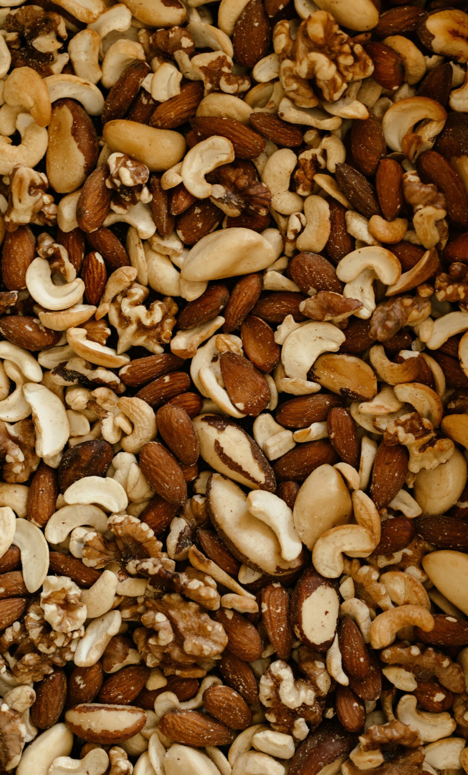 A close-up view of a mixed assortment of nuts, including almonds, cashews, walnuts, and Brazil nuts, filling the entire frame.
