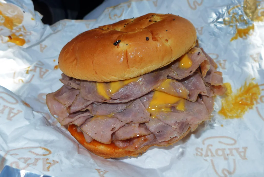 A roast beef sandwich with melted cheese on a toasted bun, wrapped in Arby's branded paper.