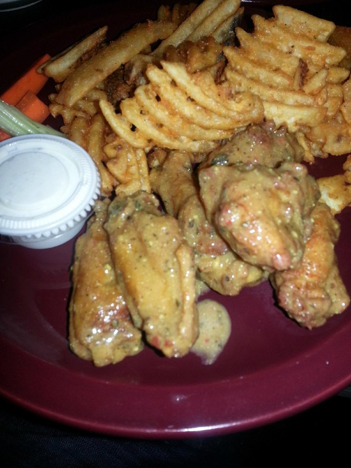 A plate with seasoned chicken wings, waffle-cut fries, celery sticks, and a small container of dipping sauce.