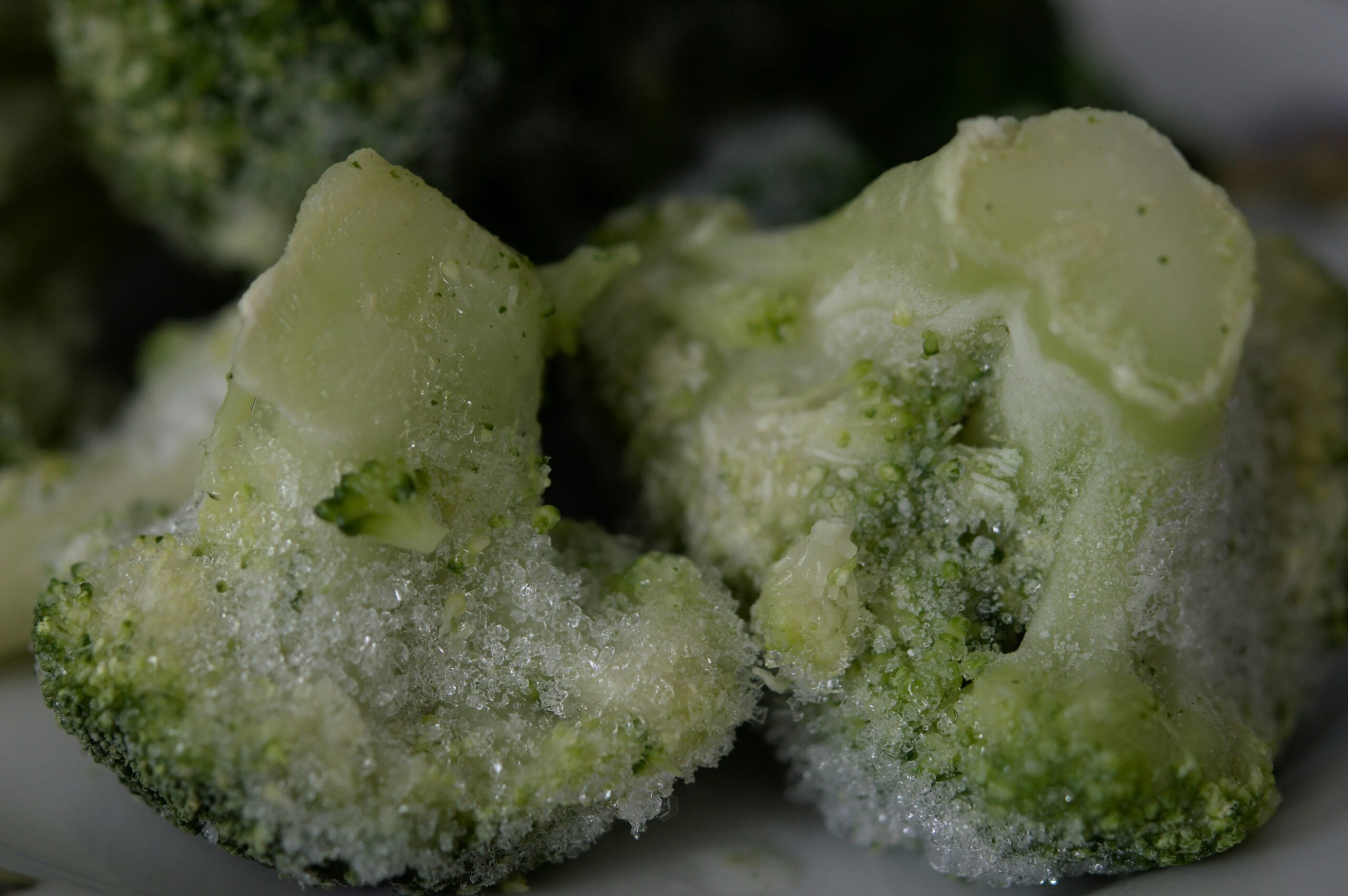 Close-up of several pieces of frozen broccoli, covered with a layer of ice crystals, highlighting their green color and frosty texture.