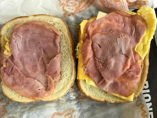 Two slices of white bread, each topped with a slice of ham; one side also has scrambled eggs and a slice of cheese, making an open-faced breakfast sandwich.