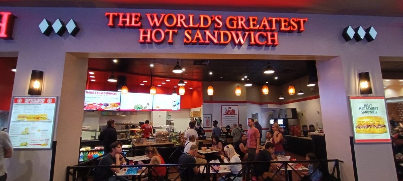 A busy sandwich restaurant with a large sign reading "THE WORLD'S GREATEST HOT SANDWICH" welcomes diners—an ideal stop for Las Vegas budget tips seekers in the well-lit, modern interior.