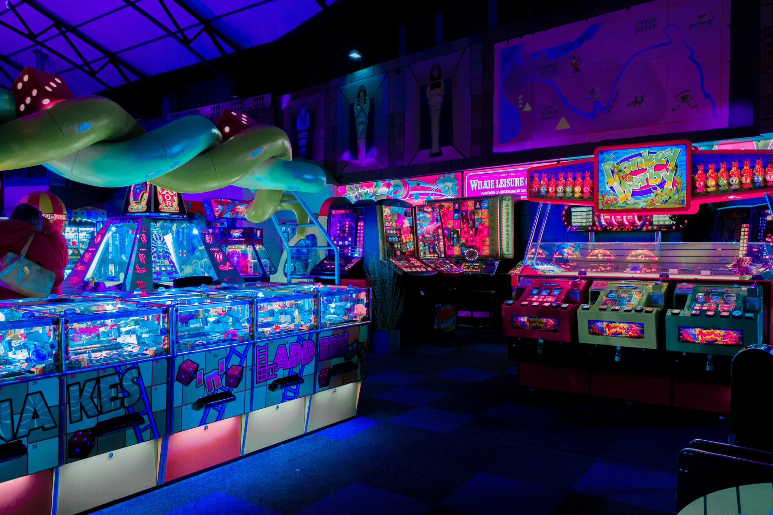 A brightly lit arcade filled with colorful neon lights, various game machines, and arcade cabinets, creating a lively and vibrant atmosphere in a dimly lit indoor space.