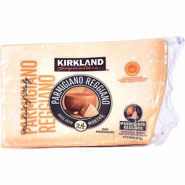 A wedge of Kirkland Signature Parmigiano Reggiano cheese, labeled "aged over 24 months" with packaging showing the cheese’s rind and logo. The cheese is vacuum-sealed in plastic.