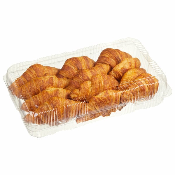 A clear plastic container holds several golden-brown croissants arranged in two rows, viewed on a white background.
