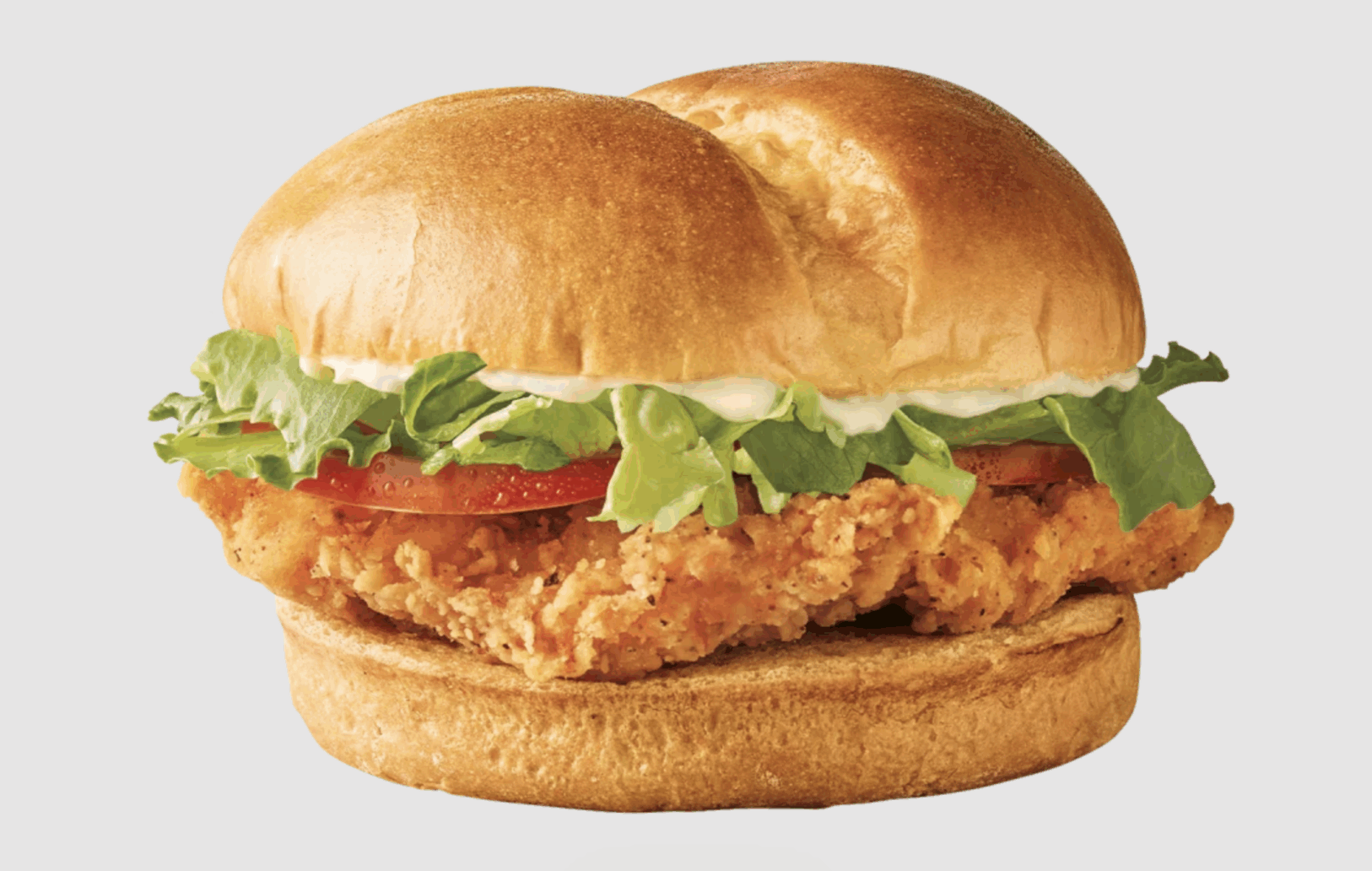 A crispy Chicken Sandwich with lettuce, tomato, and mayonnaise on a golden toasted bun, set against a plain light background.