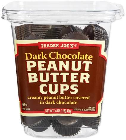 A clear plastic tub labeled "Trader Joe’s Dark Chocolate Peanut Butter Cups" contains individual chocolate cups with creamy peanut butter filling, covered in dark chocolate. The container holds 16 ounces (1 lb) of candy.